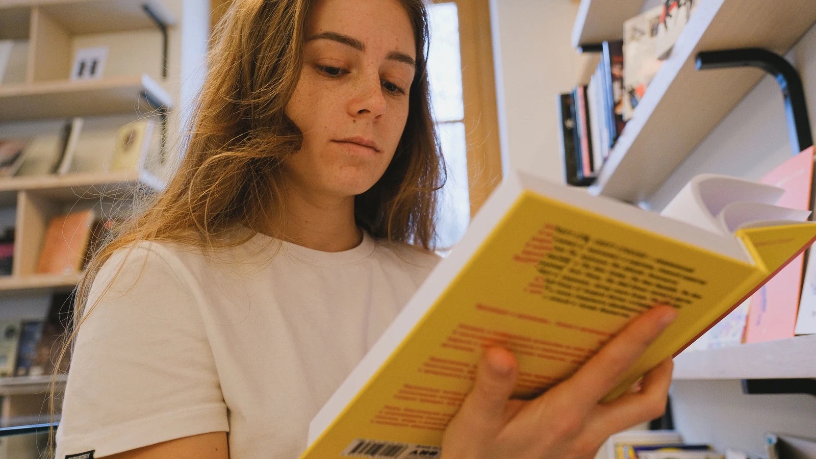Взрослая женщина читает книгу среди книжных полок.